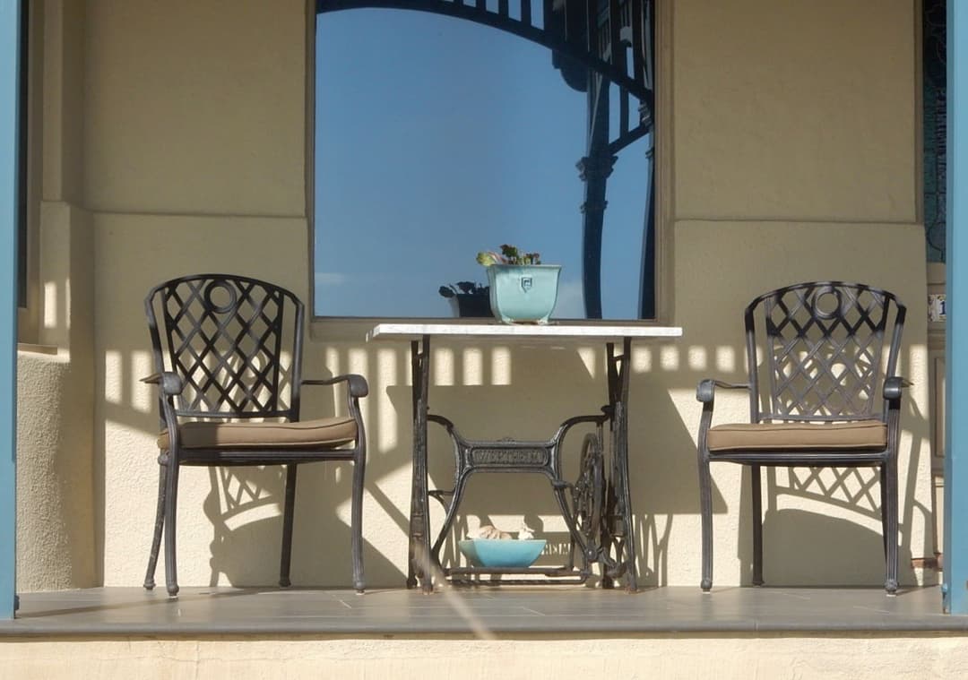 An old treadle sewing machine base with a stone top, used as a small verandah table between two chairs