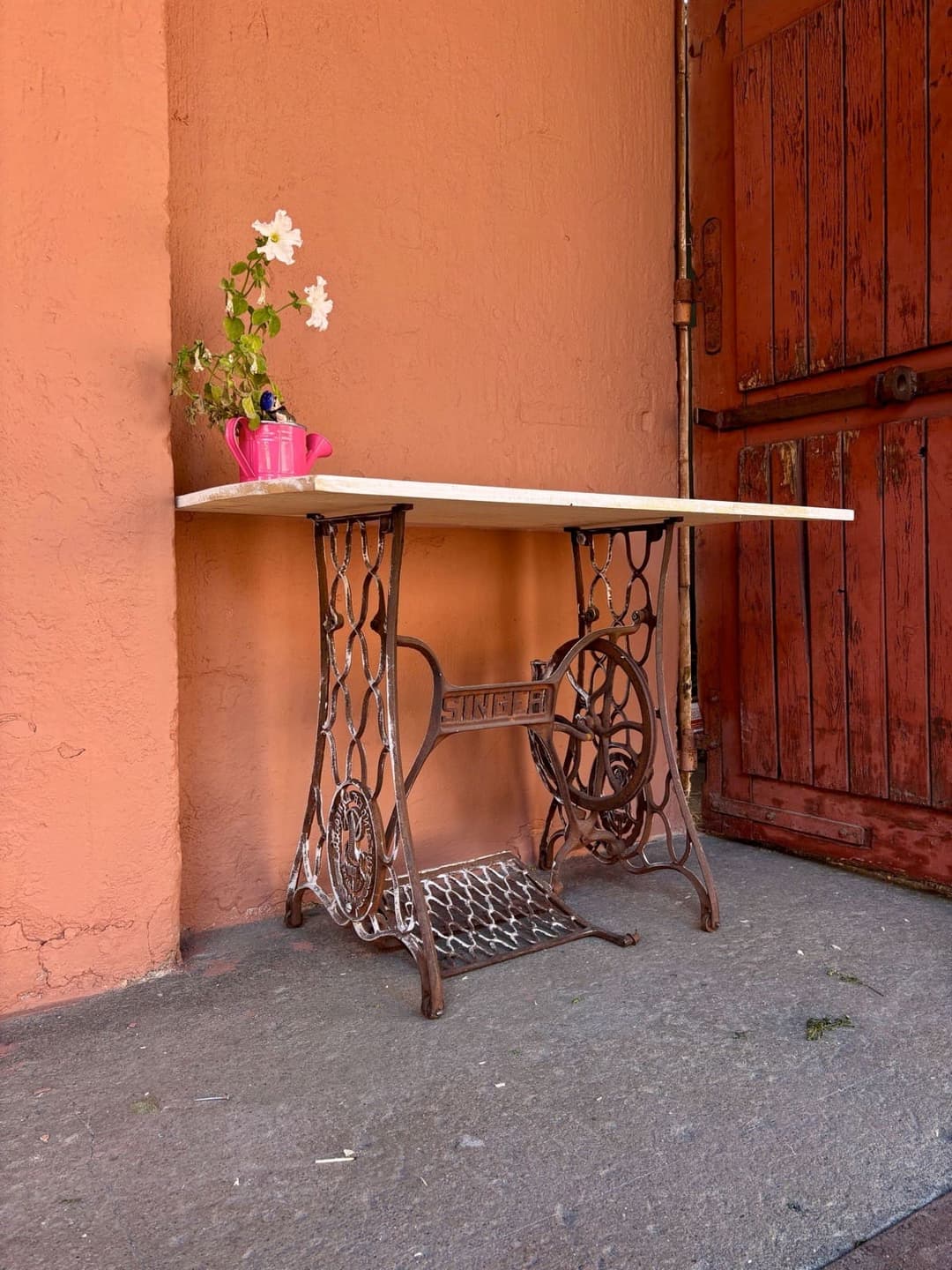 A treadle sewing machine base with a pale stone top, used as a small table against a painted wall
